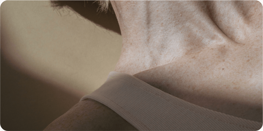 Крупный план шеи и плеча пожилого человека. Мягкое освещение подчеркивает морщины и веснушки. Спокойный тон, отражающий естественное старение.